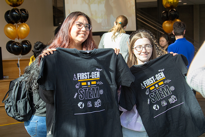 Two first generation students hold up t-shirts that read "First-Gen in STEM"